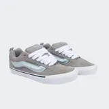 Championes Vans modelo Knu Skool de corte bajo, con diseño robusto inspirado en los años 90. Presentan capellada de gamuza gris, lengüeta y cuello acolchados, cordones anchos blancos y la icónica Sidestripe 3D en color celeste. Incluyen suela vulcanizada blanca con diseño waffle.
