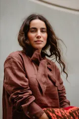 Blusa de lino color marrón con cuello tipo lazo, mangas largas y diseño entallado con pinzas frontales.