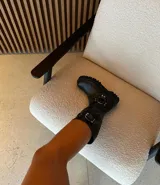 Bota de caña alta negra de cuero encerado con hebillas en la caña, herrajes de níquel y suela artesanal negra.