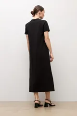 Vestido midi negro de manga corta y cuello redondo, con detalles de botones plateados en el hombro izquierdo, tajo lateral y un cinturón fino ajustable con hebilla metálica.