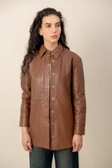 Camisa de cuero 100% color marrón, de corte largo y recto, con cuello camisero y cierre frontal de broches metálicos.