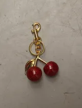 Llavero dorado con dije de cerezas rojas brillantes.