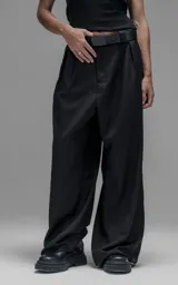 Pantalón sastrero de corte oversize, color negro, con pinzas frontales que forman tablones profundos, cintura ancha, presillas robustas y bolsillos laterales y traseros tipo ojal.