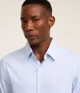 Camisa de manga larga color celeste, con cuello inglés y abotonado delantero. Confeccionada en tricolina con fibra de bambú, presenta un diseño maquinetado con estampado de rayas.