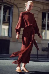 Vestido largo fluido en color bordó, confeccionado en georgette. Presenta cuello redondo, mangas largas con pliegues terminadas en puños y tiras ajustables para atar en la cintura. Incluye forro interior a tono.