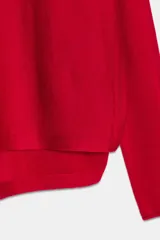 Jersey de punto color rojo vibrante, con cuello barco y manga larga. Presenta un calce amplio estilo capa con bajo asimétrico y aberturas laterales.