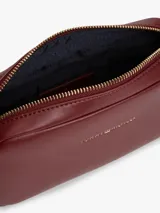 Cartera bandolera Tommy Hilfiger modelo Essential de color bordó, con acabado liso, cierre de cremallera y correa ajustable de jacquard. Presenta el logo y la inscripción de la marca en bajo relieve en la parte delantera.