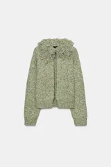 Chaqueta de punto de textura jaspeada en color verde, con cuello redondo adornado con flecos del mismo tejido, manga larga y cierre frontal con corchete metálico.