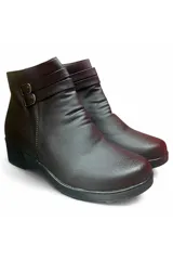 Bota corta de cuero color marrón, con taco bajo, puntera redondeada y diseño fruncido en el empeine. Presenta dos tiras decorativas cruzadas en el lateral exterior con hebillas metálicas doradas.