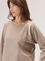 Camisa de manga larga con diseño bicolor en tonos tierra. Presenta un panel frontal y trasero en color beige, contrastado con mangas de un tono marrón más oscuro y textura satinada. Posee cuello redondo y corte recto.