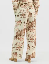 Conjunto de dos piezas compuesto por camisa de manga larga con cuello solapa y botones frontales, y pantalón de tiro alto con pierna recta y bolsillos laterales. Ambas prendas presentan un estampado paisajístico en tonos marrones sobre fondo crema.