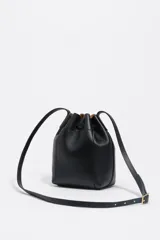 Bolso tipo saco de tamaño pequeño confeccionado en piel vacuna negra, con cierre de cordón ajustable, asa larga regulable y logo de la marca en letras metálicas doradas en la parte frontal.