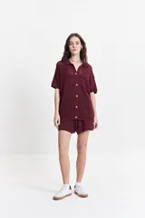 Camisa tejida color borgoña con textura calada, cuello clásico, botones y mangas cortas con elástico.