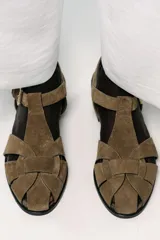 Zapato plano tipo cangrejera de mujer, color verde militar, confeccionado en serraje (gamuza). Presenta tiras trenzadas en la parte delantera y cierre con hebilla metálica en el tobillo.