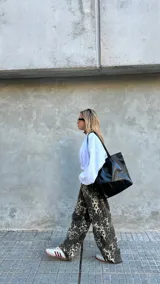 Cartera tipo shopper de cuero negro con acabado brillante, diseño amplio, doble asa de hombro y cierre superior.