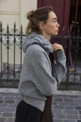 Chaqueta de punto con capucha, manga larga y cierre frontal con cremallera. Presenta un diseño en color beige con un lazo decorativo a contraste en color marrón oscuro en la zona del cuello.