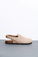 Sandalias estilo zueco color beige con tira trasera ajustable, hebillas metálicas plateadas, suela de corcho y base de goma negra.