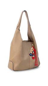 Cartera tipo hobo de cuero sintético color suela, con interior espacioso y costuras decorativas frontales. Incluye asa de hombro fija, monedero rectangular colgante a juego y un llavero amuleto con cuentas de madera, ojos turcos y detalles en rojo.