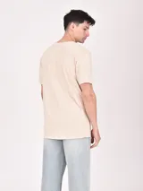 Remera color beige con estampa rectangular con diseño abstracto en tonos marrones y texto.