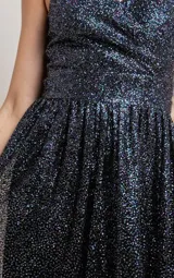 Vestido largo de fiesta con escote en V cruzado y tirantes finos. Confeccionado en tela negra con acabado de glitter brillante, presenta un corte entallado en la cintura y falda con caída fluida.