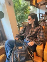 Camisa de corte oversize con estampado de cuadros escoceses en tonos negro y marrón. Presenta cuello camisero, cierre frontal con botones y mangas largas con volumen y puños elásticos.