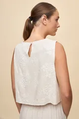 Top sin mangas color blanco con escote redondo, calce amplio y diseño con bordado floral en relieve.