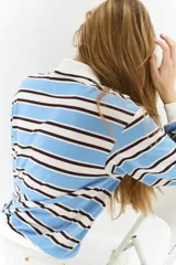 Remera polo de manga larga con cuello clásico blanco y tapeta de botones. Presenta un patrón de rayas horizontales en azul celeste, blanco y negro. Tiene remates acanalados en puños y bajo.