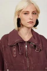 Chaqueta color borgoña de corte recto con cierre frontal metálico y cuello amplio con hebillas decorativas. Cuenta con bolsillos laterales con broches y costuras marcadas que aportan un aire utilitario.