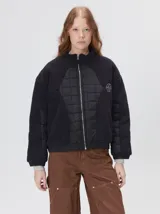 Campera crop de corte boxy y color negro, forrada en corderito, con parches capitoneados en el pecho y las mangas. Cuenta con cierre frontal metálico, cuello alto, puños y bajo elastizados, y detalle de logo bordado en hilo en el pecho.