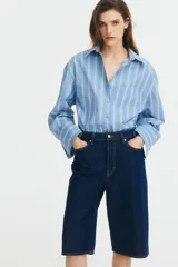 Bermuda de denim azul oscuro, tiro alto, corte ancho, largo a la rodilla y cinco bolsillos. Cierre frontal con botón.