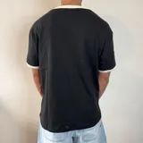 Remera de corte regular color blanco con detalles en gris oscuro en el cuello y los bordes de las mangas. Presenta un estampado pequeño centrado en el pecho.
