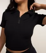 Blusa tipo polo de manga corta, color negro, con cierre frontal en el cuello y textura acanalada. Confeccionada en tejido seamless.