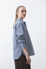 Camisa a rayas verticales blancas y marrones, de manga larga con puños abotonados, cuello camisero y botones frontales. Incluye un bolsillo en el pecho con bordado sutil.