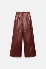 Pantalón de tiro medio confeccionado en 100% piel, con diseño de pierna ancha, cintura con trabillas, bolsillos laterales y cierre frontal con cremallera, botón y ganchos metálicos.