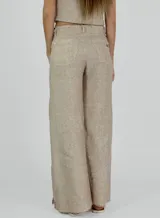 Pantalon de corte recto y pierna ancha, confeccionado en lino color beige. Presenta un diseño de tiro medio con aberturas laterales en el ruedo y detalle de bordes desflecados.