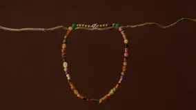 Collar largo de diseño artesanal compuesto por una variedad de cuentas de piedras naturales y materiales orgánicos en tonos tierra, naranja, verde y violeta, con cierre metálico.