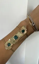 Brazalete rígido dorado con tres piedras verdes incrustadas.