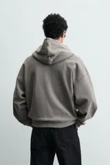 Sudadera tipo hoodie de corte relajado, confeccionada en tejido de algodón con textura estructurada y efecto lavado. Presenta cierre frontal con cremallera, cuello con capucha, manga larga, bolsillos tipo canguro y acabados en rib.