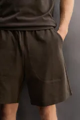 Short jogger marrón de corte relaxed fit, confeccionado en tejido compacto de algodón, con cintura elástica ajustable, bolsillos frontales en la cadera y bolsillo trasero de plastrón.