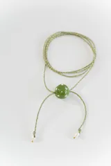 Gargantilla tipo bolo tie de tiento trenzado verde con dije esférico celeste con brillos incrustados.