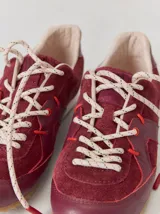 Championes de cuero en tonos bordó y rojo, con diseño de paneles combinados en gamuza y cuero texturizado. Presentan suela blanca con base dentada color caramelo y cordones jaspeados.