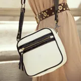 Bandolera blanca con detalles en negro, confeccionada en cuero vacuno con textura tipo piel de cocodrilo. Tiene correa larga ajustable y removible, bolsillo externo con cierre y forro interior con bolsillo con cierre.