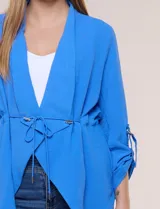 Chaqueta liviana azul de silueta fluida y diseño abierto, con solapa caída, mangas tres cuartos con presilla y argolla metálica, y ruedo irregular.