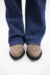 Botín de cuero vacuno color marrón, con punta fina y detalle de tachas metálicas en la parte superior. Presenta una suela de plataforma plana de color negro.