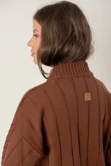 Buzo de punto color chocolate con cuello alto, mangas largas y diseño de trenzas verticales. Presenta puños y ruedo acanalados.