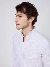 Camisa Oxford de corte regular fit, color blanco con finas rayas verticales, cuello buttondown y manga larga con puño simple. Cuenta con cierre frontal de botones y logo bordado en el pecho.