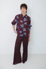 Camisa de corte clásico con cuello camisero y cierre frontal de botones, confeccionada en tela color bordó con estampado floral en tonos celestes.