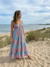 Vestido largo de verano con estampado floral en tonos celeste y rosado. Presenta un escote halter con tirantes finos que se anudan en el cuello y un corte imperio con frunces que genera una falda con mucho vuelo y volados en los ruedos inferiores.