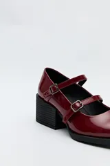Zueco estilo Mary Jane color negro charol, con doble tira y hebillas metálicas. Presenta punta cuadrada y taco ancho de altura media.