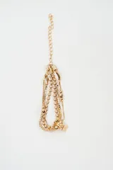 Brazalete multicapa de color dorado compuesto por cadenas de eslabones tipo caja y cadenas de esferas pequeñas, con un dije en forma de cubo en el extremo.